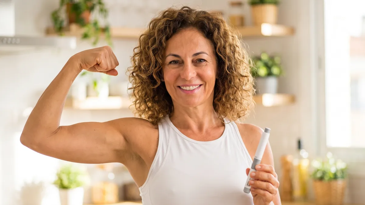Mujer feliz con una pluma de tratamiento GLP-1 mostrando el músculo del brazo