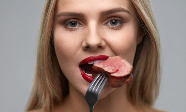 Woman Eating Meat. Closeup of Healthy Hungry Girl With Beautiful Face, Red Lips Eats Delicious Grilled Meat. Female Mouth Biting Piece Of Tasty Beef Steak On Fork. Nutrition Concept. High Resolution